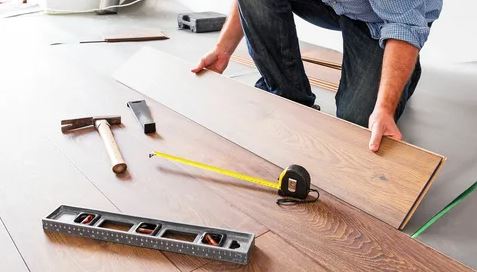 A man using tools to work on a wooden floor, focused on his task in a well-lit environment.