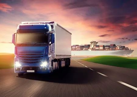 A truck transporting cargo containers travels along a road, showcasing logistics in motion.