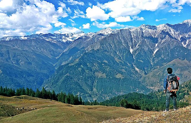 Trekker standing atop a mountain on Bhrigu Lake Trek, soaking in panoramic views of the Himalayas and the serene alpine atmosphere